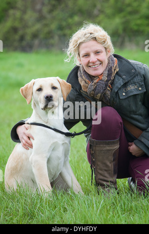 A woman wearing shooting or riding clothing outside with a yellow labrador retriever dog in the countryside Stock Photo