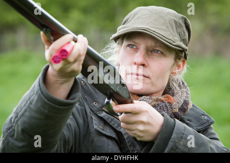 A woman wearing shooting clothing and standing outside in the English countryside with a shotgun Stock Photo