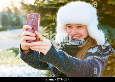 Portrait of teenage girl taking selfie picture with mobile phone outside in winter Stock Photo