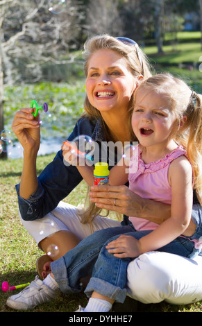 mother and daughter blowing bubbles in park Stock Photo