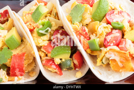 Tacos filled with migas, a Tex-Mex dish of eggs scrambled with red bell pepper, onions, jalapenos, cheese, topped with avocado Stock Photo