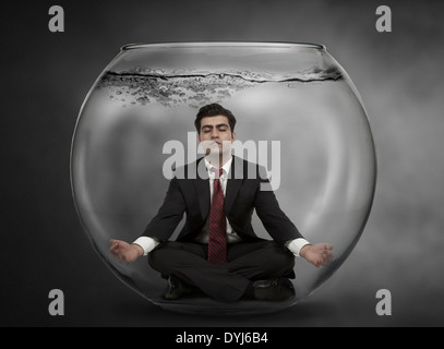 Business man meditates under water in a fish bowl Stock Photo