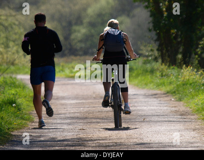 Fit couple, Man jogging and woman cycling beside him on the Camel trail between Wadebridge and Bodmin, Cornwall, UK Stock Photo