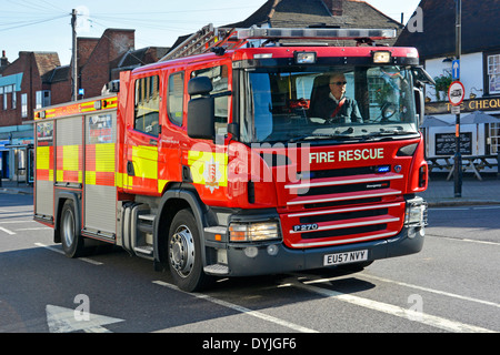 Essex Fire and Rescue lorry truck fire brigade engine appliance crew on emergency call driving along shopping high street Billericay Essex England UK Stock Photo