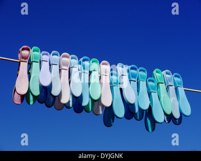 Abstract image showing colourful plastic clothes pegs on a washing line, against bright blue sky Stock Photo