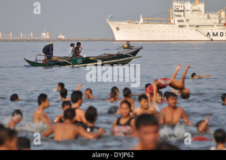 Manila, Philippines. 20th April, 2014.  Fishermen onboard a boat pass by Filipinos swimming the polluted water of Manila Bay during the celebration of Easter in Manila on Sunday, April 20. Despite city-imposed swimming banning, many poor Filipinos still swam the bay waters to cool themselves from the summer heat.  Photo: Jay Ganzon/Pacific Press/Alamy Live News Stock Photo