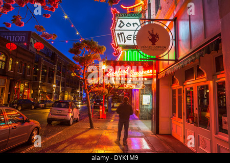 Man standing on street outside Chinese restaurant lit up at night-Victoria, British Columbia, Canada. Stock Photo