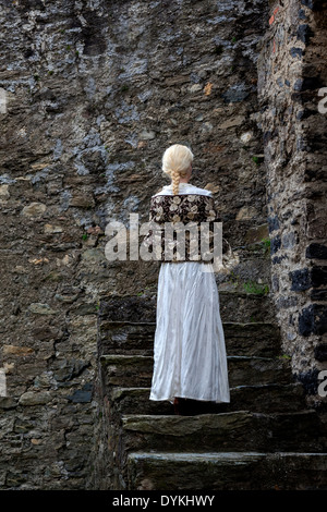 a lady in a white period dress is standing on old stone steps Stock Photo