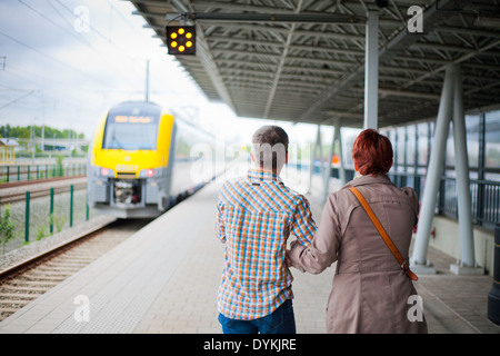 Parents standing on the platform in a railway station waving goodbye as the train with their child leaves the station. Stock Photo