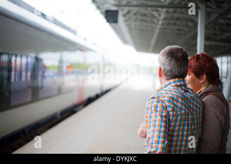 Parents standing on the platform in a railway station waving goodbye as the train with their child leaves the station. Stock Photo