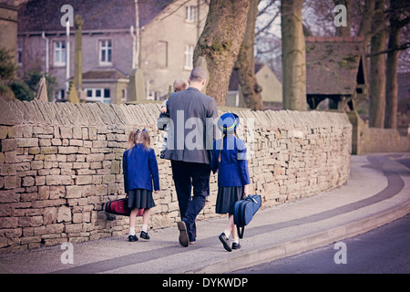 A smartly dressed father, holding hands with his children and walking them to school Stock Photo