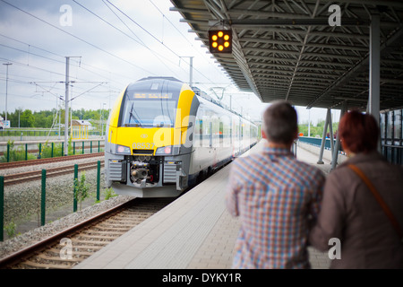 Parents standing on the platform in a railway station waving goodbye as the train with their child leaves the station. Stock Photo