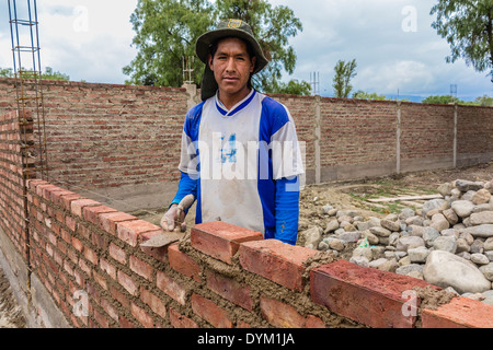 A Bolivian male mason is standing by the brick wall of a house he is constructing in Cochabamba, Bolivia. Stock Photo
