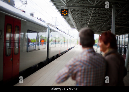 Parents standing on the platform in a railway station waving goodbye as the train with their child leaves the station. Stock Photo