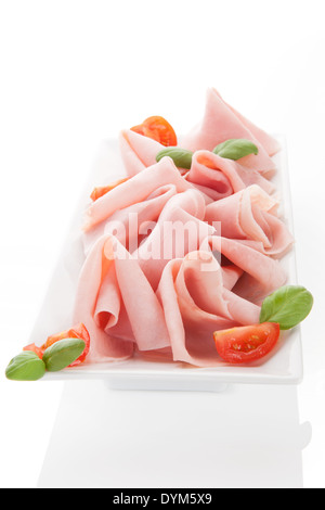 Ham slices on white tray with basil leaves and tomatoes. Culinary meat eating. Stock Photo