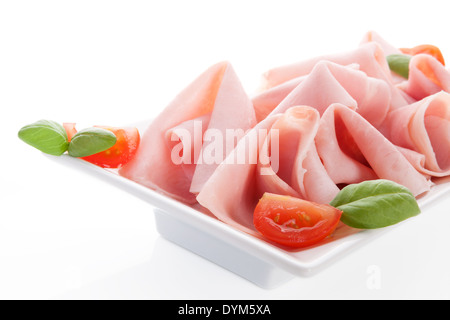 Delicious ham close up with fresh basil leaves and tomatoes on white plate isolated on white background. Culinary meat eating. Stock Photo