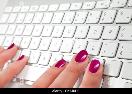 Female finger with red fingernail touching silver and white keyboard, selective focus. Help desk concept. Stock Photo