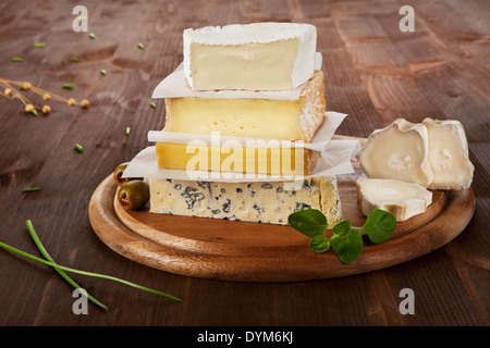 Various cheese sorts on wooden board with olives, wheat and chive. Stock Photo