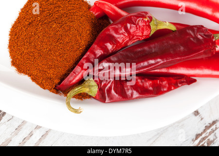 Fresh, dry chili peppers and paprika powder spice on white plate on white wooden background. Culinary cooking spices. Stock Photo
