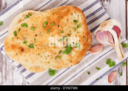 Garlic coriander naan pile on kitchen cloth on white wooden textured background with fresh herbs and garlic. Stock Photo