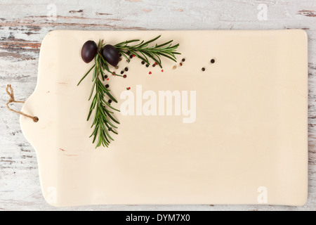 Empty ceramic kitchen board with rosemary and peppercorns in the corner on white wooden textured background as your copy space, Stock Photo