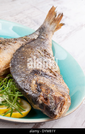 Grilled sea bream fish on plate with fresh rosemary and lemon. Culinary healthy seafood eating. Stock Photo