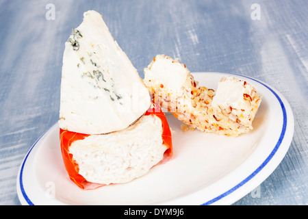 Luxurious colorful cheese assortment. Blue cheese, cream cheese and goat cheese on plate on blue wooden background. Culinary Stock Photo