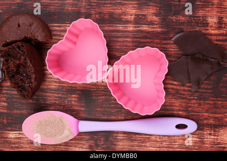 Baking delicious muffins. Chocolate baking mixture, fresh muffins and pink heart shaped baking forms on brown wooden background, Stock Photo