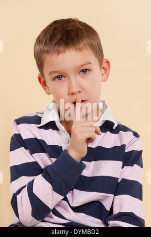 The secret. Don't tell anyone. Young sad boy with finger over his mouth isolated on neutral background. Facial expressions Stock Photo