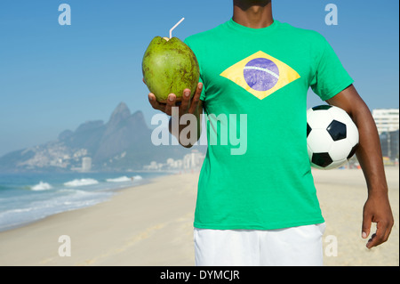 Brazilian soccer player in Brazil t-shirt holding football and drinking coconut Rio de Janeiro Stock Photo