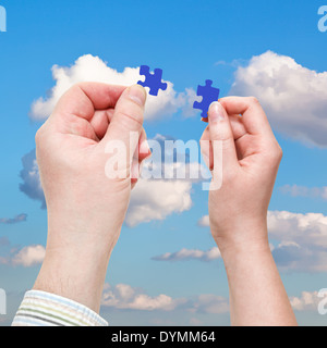 male and female hands with little puzzle pieces with white clouds in blue sky background Stock Photo