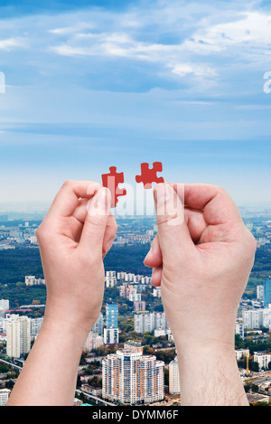 male and female hands with little puzzle pieces with modern urban residential district background Stock Photo