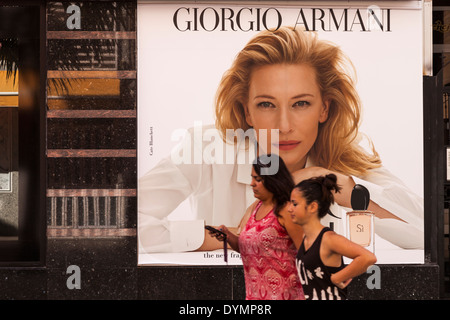 Women walking past a Giorgio Armani perfume ad in Los Cristianos, Tenerife, Canary Islands, Spain. Stock Photo