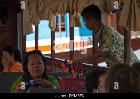 Horizontal portrait of an Asian lady buying snacks from a local boy on a slowboat up the Mekong river. Stock Photo