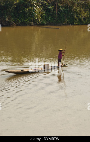 Vertical view of a traditionally dressed Asian lady punting a long boat down the Mekong river on a sunny day. Stock Photo