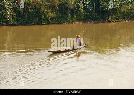 Horizontal view of a traditionally dressed Asian lady punting a long boat down the Mekong river on a sunny day. Stock Photo