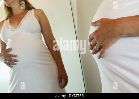 A close up of a pregnant woman looking at herself in the mirror. Stock Photo