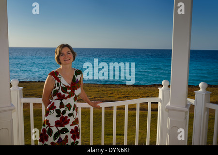 Woman vacationer standing at a railing by the sea at a Varadero Cuba resort hotel on Bay of Cardenas Atlantic ocean Stock Photo
