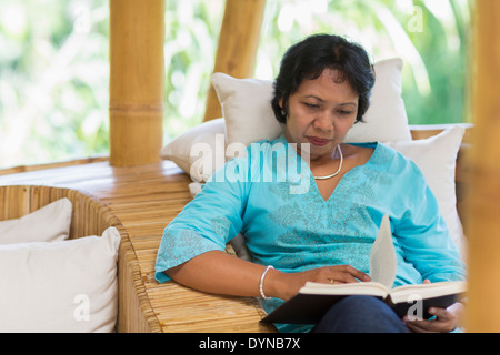 Balinese woman reading in armchair Stock Photo