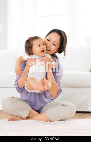 Mother playing with baby girl in living room Stock Photo