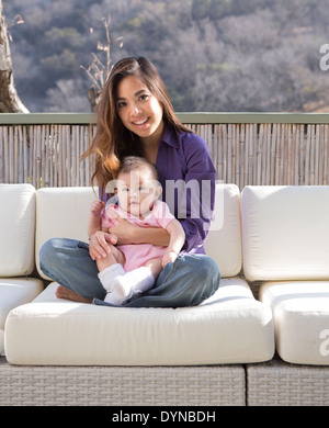 Mother holding baby girl on patio sofa Stock Photo