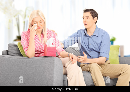 Young husband comforting his sad wife seated on sofa at home