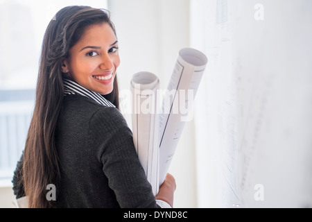 Hispanic architect carrying blueprints in office Stock Photo