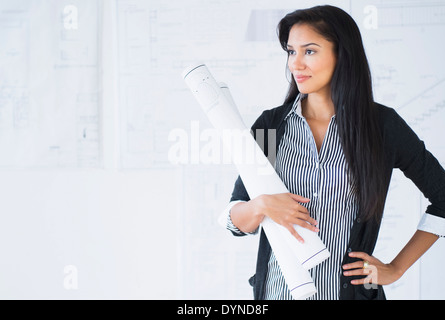 Hispanic architect carrying blueprints in office Stock Photo