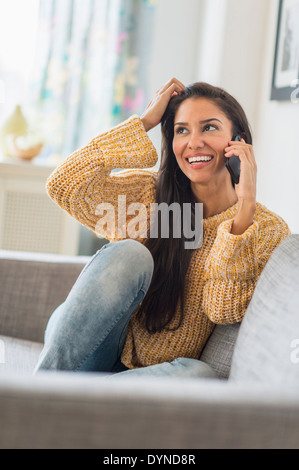 Hispanic woman talking on cell phone on sofa Stock Photo
