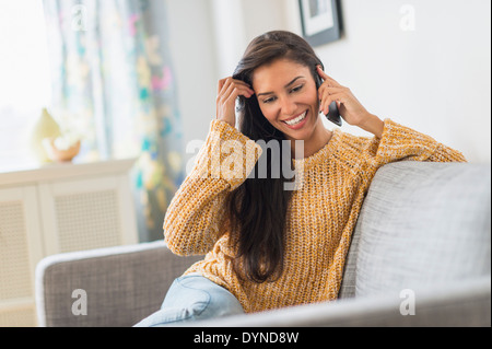 Hispanic woman talking on cell phone on sofa Stock Photo