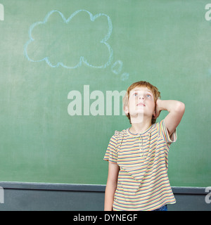 Boy in elementary school thinking with thought bubble drawn on chalkboard Stock Photo