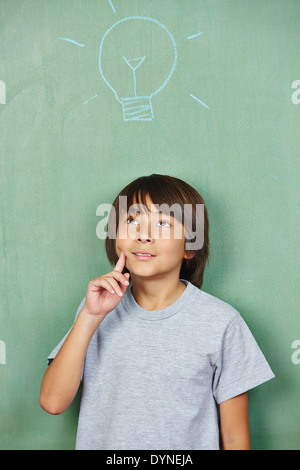 Pensive japanese boy with lightbulb drawn on chalkboard in school Stock Photo