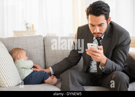 Father sitting with baby and using cell phone Stock Photo