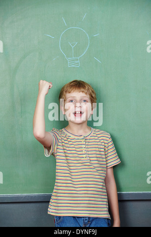 Cheering boy has idea with lightbulb drawn on chalkboard Stock Photo